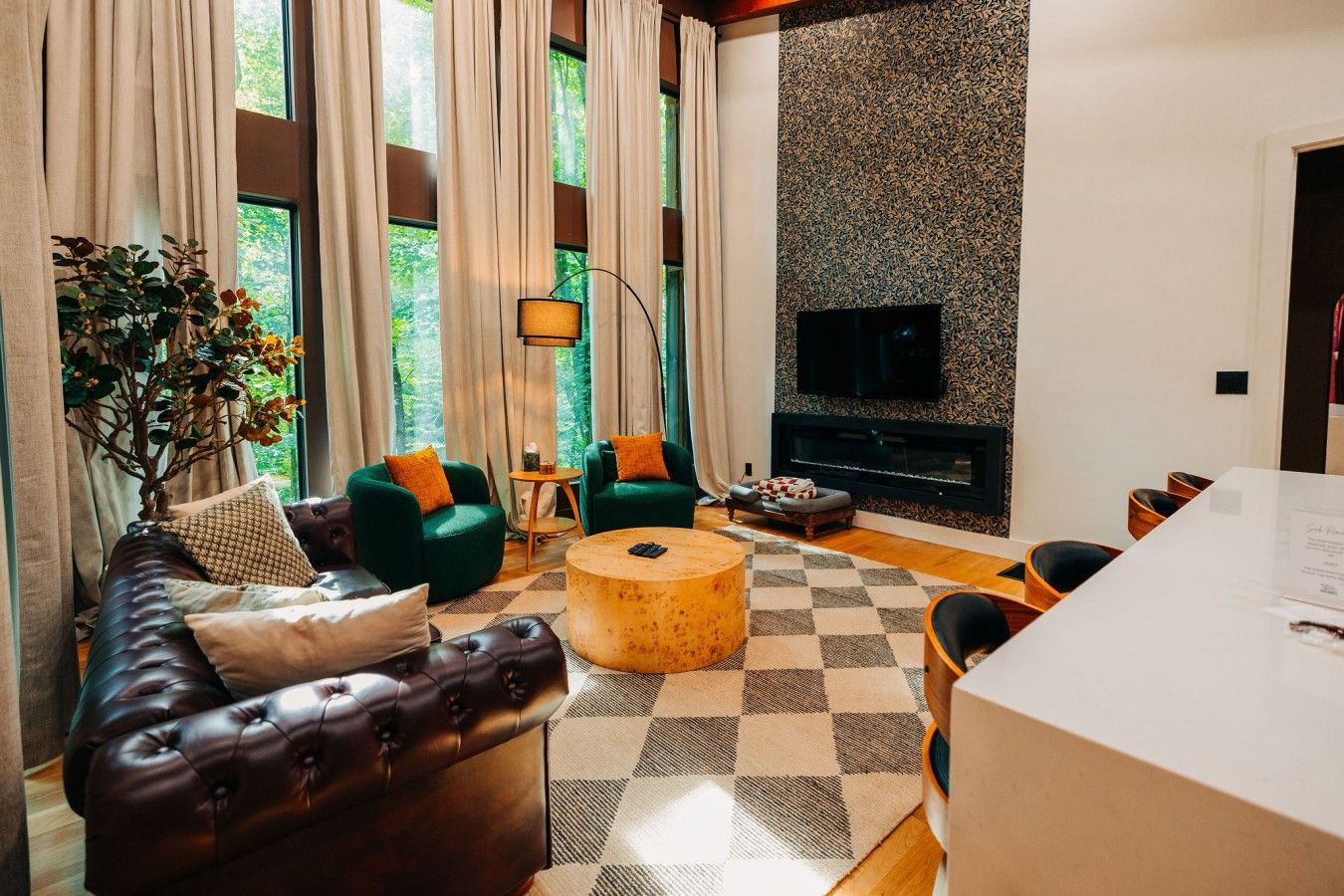 A living room with a fireplace, green armchairs, a leather sofa, and a checkered rug.
