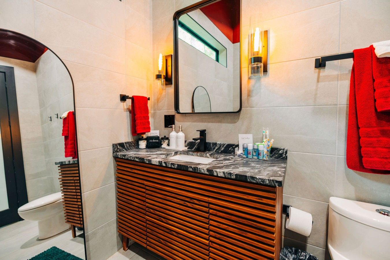 A modern bathroom with a wooden vanity, a large mirror, and a red towel on the wall.