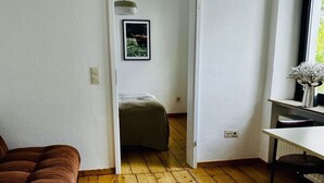 Et værelse med trægulv, en seng i baggrunden, et skrivebord med stol og et vindue med udsigt.