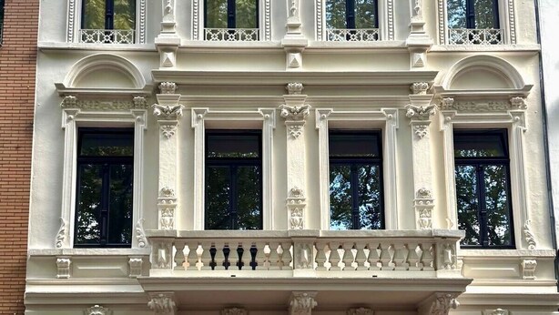 En historisk bygning med detaljeret arkitektur, herunder søjler, dekorative gerichter og en balkon med balustrade.