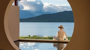 A person sitting by a circular window overlooking a body of water and mountains. - Dali Kongshanyu Fengmian Seaview Hotel (Dali)