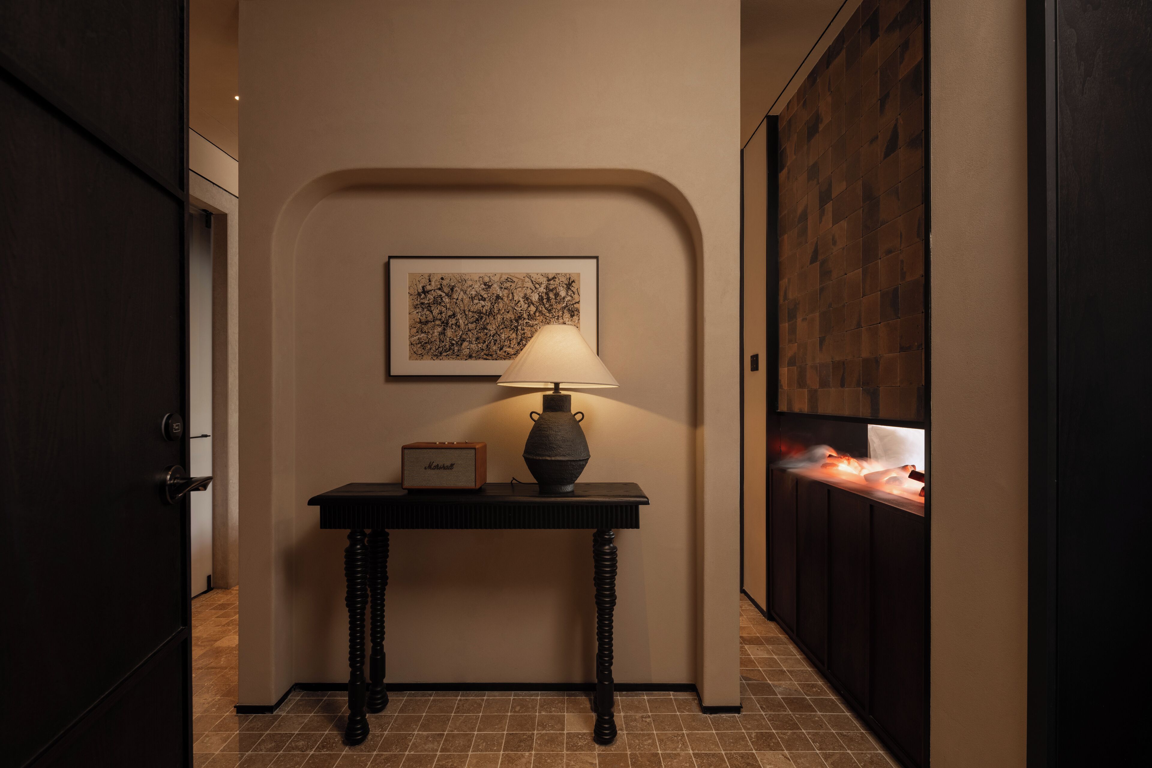 A hallway with a table lamp, a framed picture on the wall, and a tiled floor.