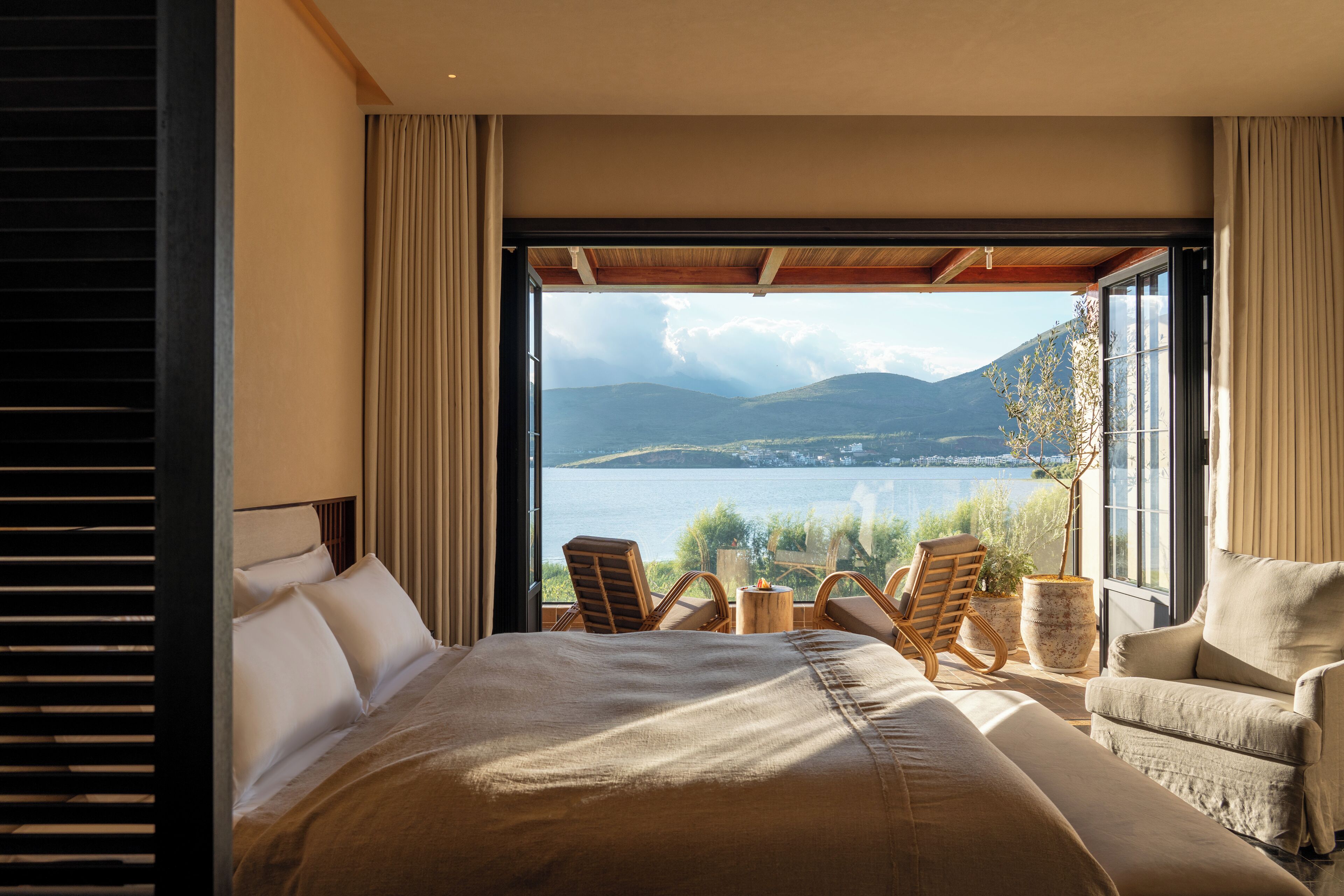 A bedroom with a large bed, two chairs, a small table, and a view of a lake and mountains.