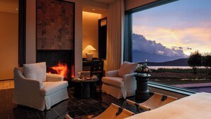 A modern hotel room with a fireplace, two armchairs, a coffee table, and a large window offering a scenic view of the landscape. - Dali Kongshanyu Fengmian Seaview Hotel (Dali)