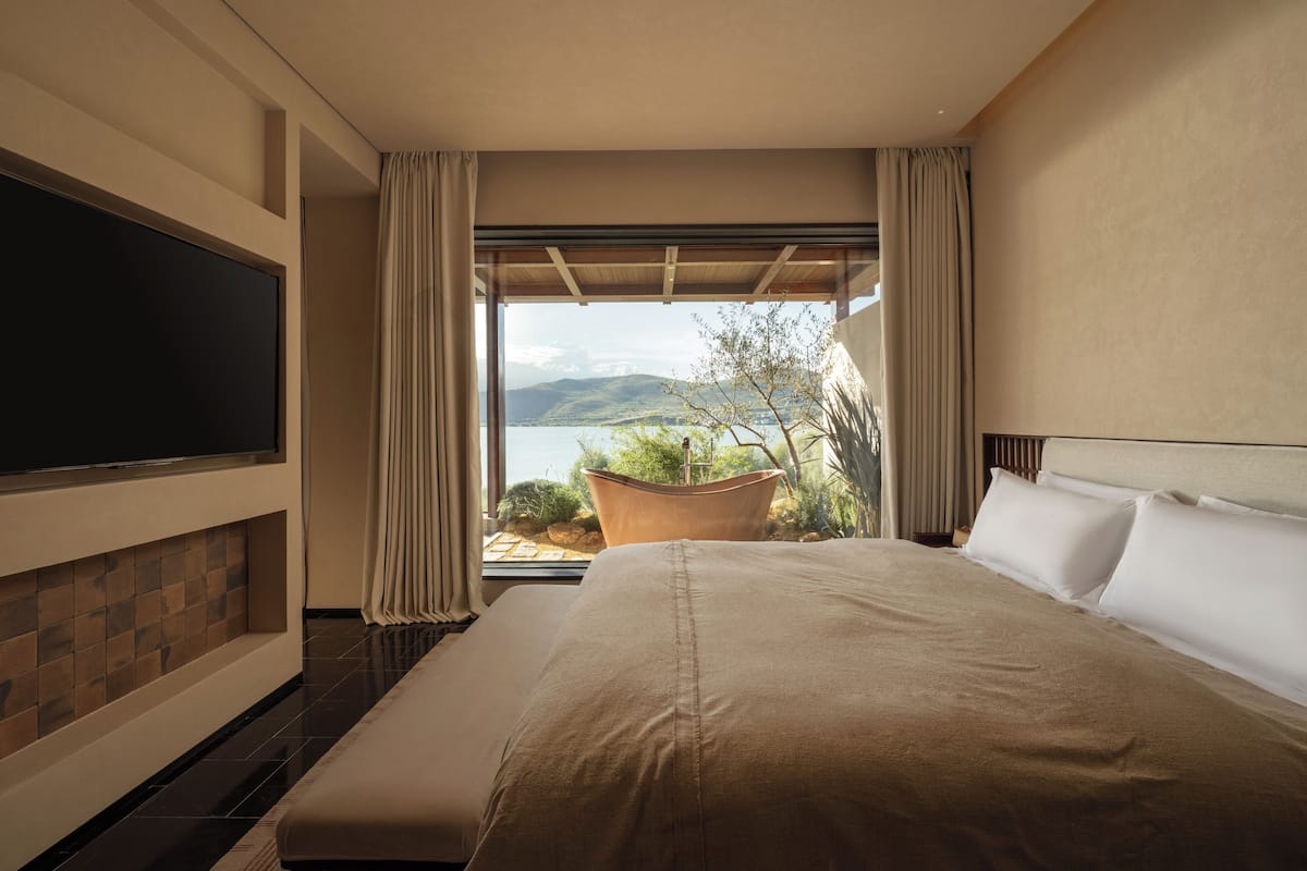 Habitación de hotel con una cama grande, un televisor de pantalla plana y vistas a un lago y montañas.