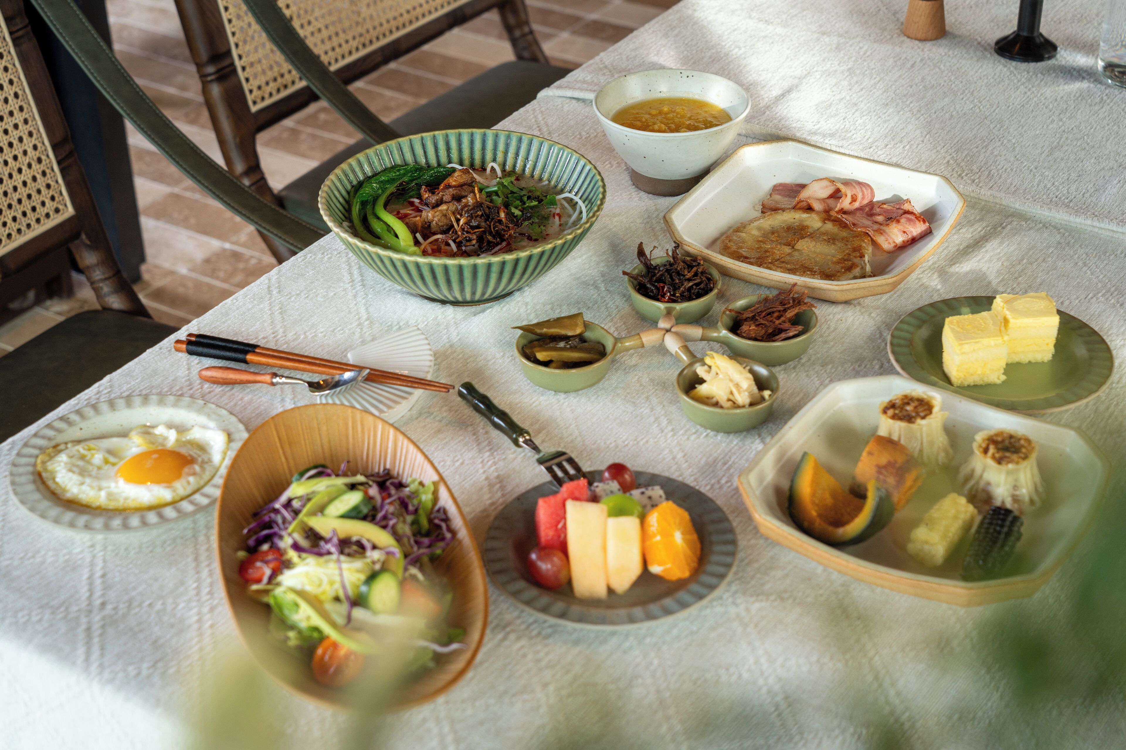 Una mesa servida con varios platos, incluyendo un tazón de ensalada, una fuente de fruta y un tazón de sopa.