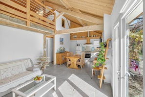 A spacious living area with a high ceiling, wooden beams, a dining table, and a sofa.