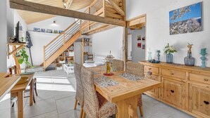 Un espace repas avec une table en bois, des chaises en osier et un escalier menant à un niveau supérieur.
