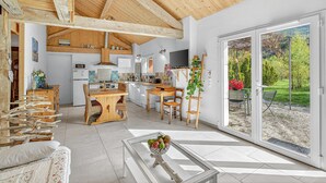 Un vaste espace de vie doté d’un haut plafond, de poutres apparentes, d’une table basse en verre et d’une porte-fenêtre coulissante donnant sur un jardin.