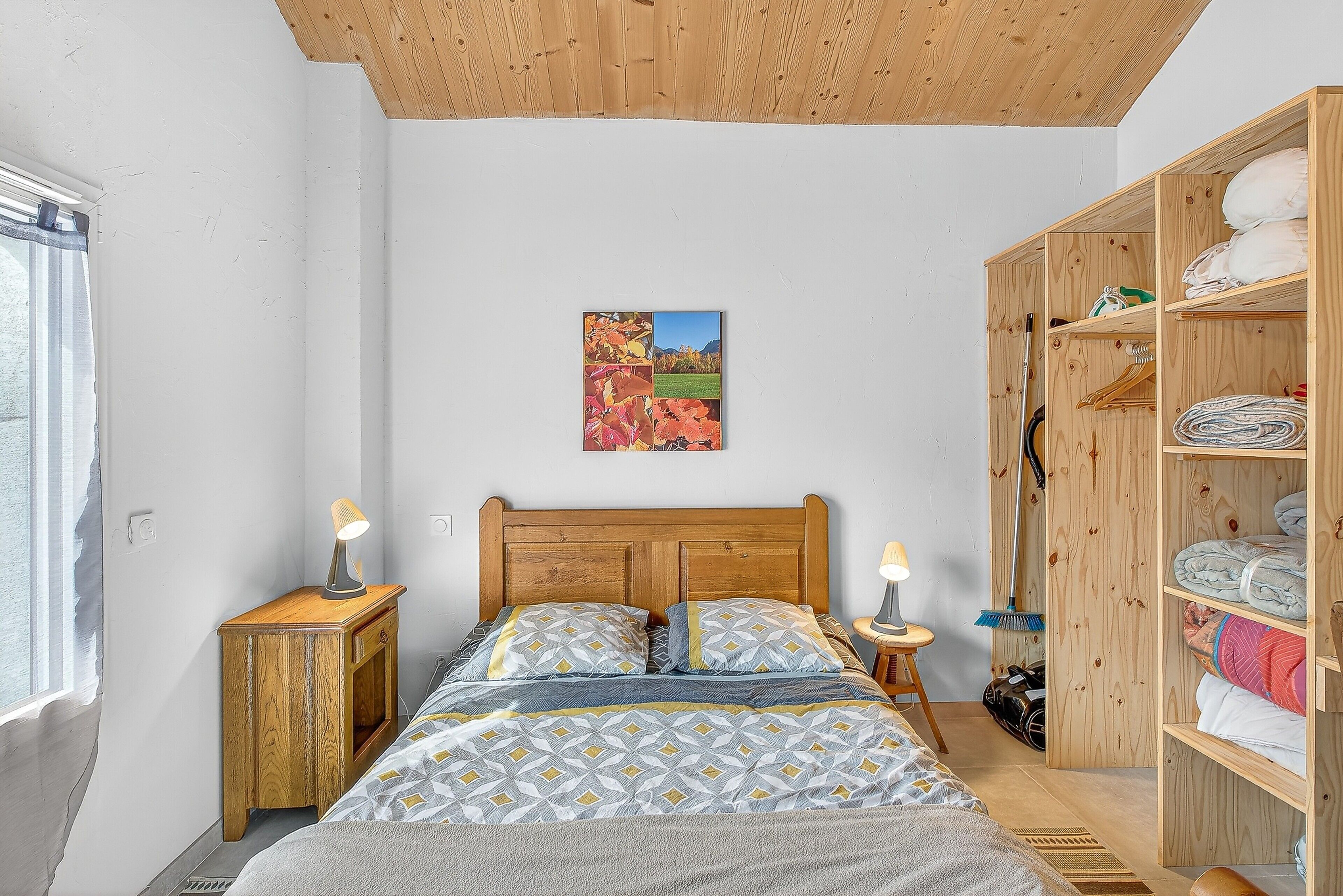 Une chambre à coucher avec une tête de lit en bois, un lit recouvert d’une literie à motifs, une armoire en bois et un tableau accroché au mur.