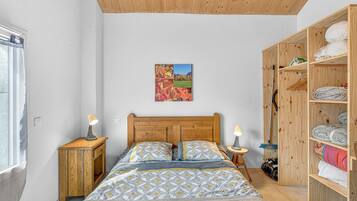 Une chambre à coucher avec une tête de lit en bois, un lit recouvert d’une literie à motifs, une armoire en bois et un tableau accroché au mur.