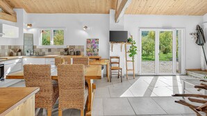 Une cuisine moderne avec des meubles en bois, un coin repas avec des chaises en osier et une grande porte-fenêtre coulissante donnant sur un jardin.