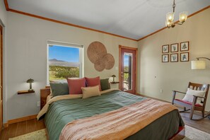 A bedroom with a large bed, a window with a view, a door, and a chair. - Retro-Modern, Mountain Retreat with 3 bedrooms, 2 baths, a bonus game room, office, and a beautiful deck with ample seating for enjoying the Stunning Mountain Peak Views. Best Views in town. (Pagosa Springs)