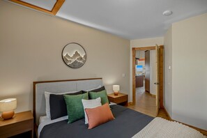 A bedroom with a bed, pillows, a bedside lamp, and a wall-mounted artwork.