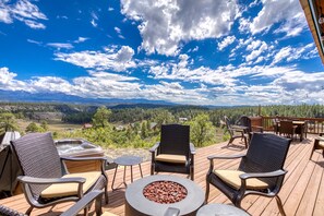 A deck with outdoor furniture, a fire pit, and a scenic view of a valley and mountains.