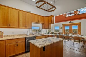A spacious kitchen with wooden cabinets, a central island, and a view of the mountains through the windows. - Retro-Modern, Mountain Retreat with 3 bedrooms, 2 baths, a bonus game room, office, and a beautiful deck with ample seating for enjoying the Stunning Mountain Peak Views. Best Views in town. (Pagosa Springs)