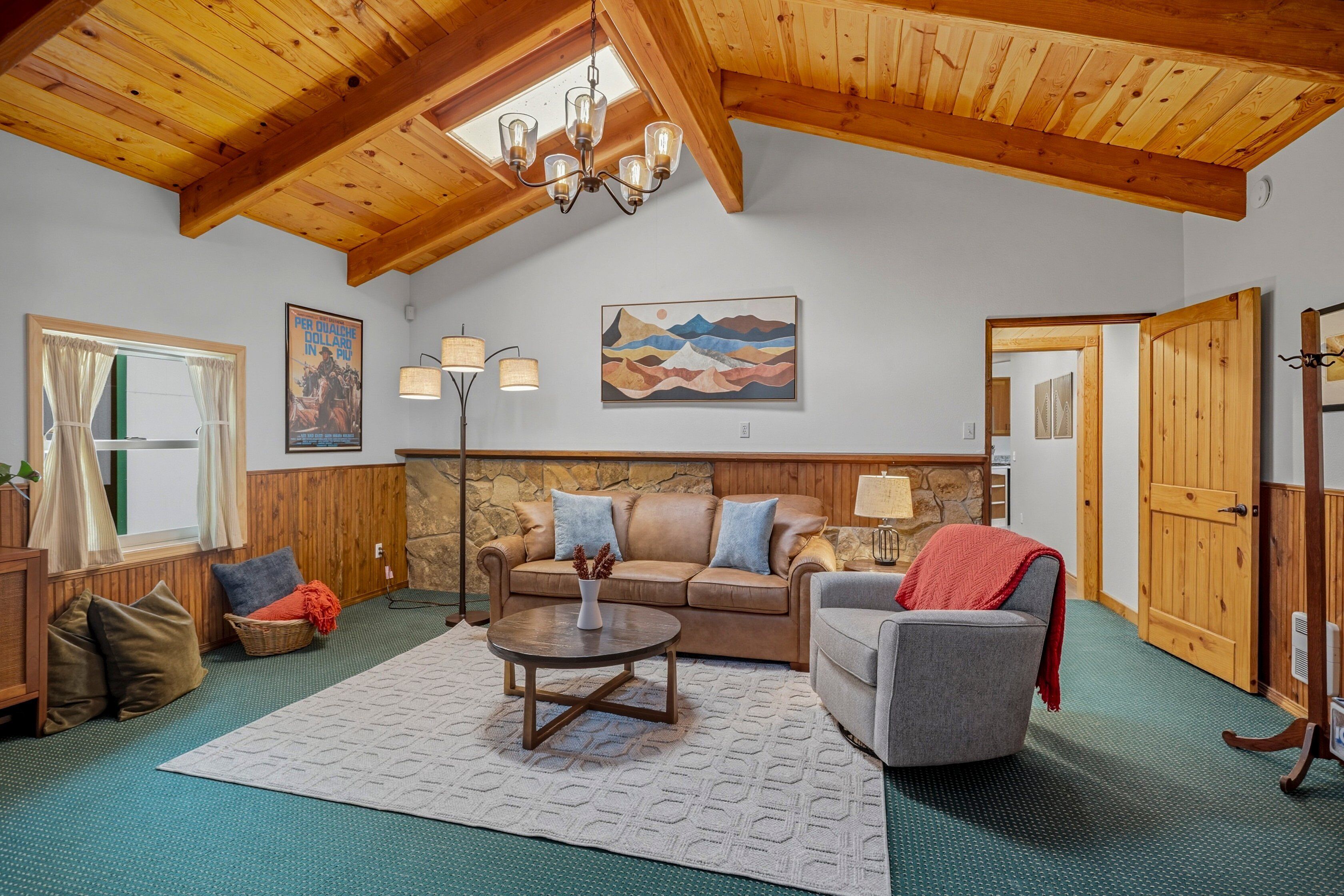 A cozy living room with a high wooden ceiling, a stone wall, a large sofa, a coffee table, and a fireplace.