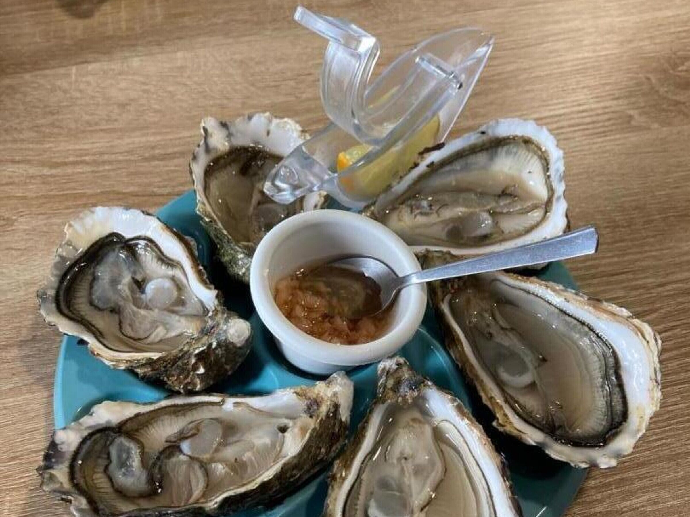 A plate of oysters with a dipping sauce and lemon wedges.