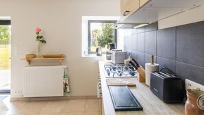 A modern kitchen with a built-in stove, a coffee machine, and a toaster. There is a window providing natural light and a view of the outdoors. - Charming stone house with garden near the sea (Quettreville-sur-Sienne)