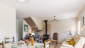 A dining area with a table set for four, a sofa, and a fireplace. - Charming stone house with garden near the sea (Quettreville-sur-Sienne)