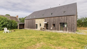 A modern farmhouse with a stone foundation, large wooden barn, and a spacious backyard with outdoor seating. - Charming stone house with garden near the sea (Quettreville-sur-Sienne)