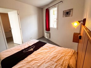 A bedroom with a bed, a window with red curtains, a radiator, and a wall-mounted light fixture. - Spacious apartment for 7, close to the slopes in Super Besse (Besse-et-Saint-Anastaise-Super Besse)