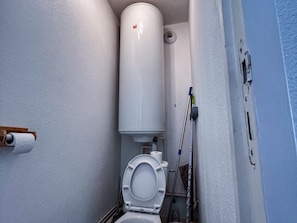 Un baño pequeño con un inodoro, un tanque blanco y un rollo de papel higiénico.