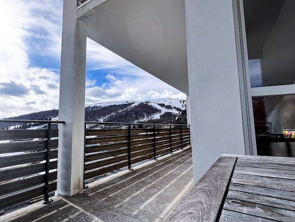 Un balcón con vista a montañas nevadas bajo un cielo parcialmente nublado.