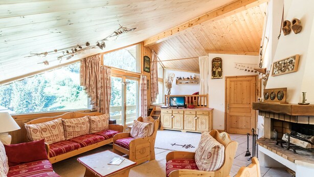 A cozy wooden cabin interior with a sofa set, a dining table, and a fireplace. - Spacious 3-bedroom ski-in apartment with parking (Méribel)