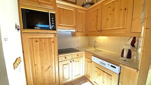 A kitchen with wooden cabinets, a microwave, a sink, and a coffee maker. - Spacious 3-bedroom ski-in apartment with parking (Méribel)