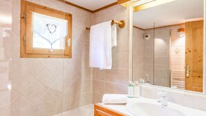 A modern bathroom with a bathtub, a large mirror, and a wooden vanity. - Spacious 3-bedroom ski-in apartment with parking (Méribel)