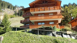 A multi-story wooden building with balconies, set in a mountainous area with trees and a clear sky. - Spacious 3-bedroom ski-in apartment with parking (Méribel)