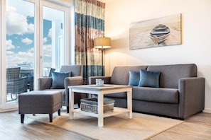 Uma sala de estar moderna com um sofá cinzento, uma poltrona a combinar e uma mesa pequena com uma luminária.