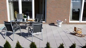 Un patio al aire libre con una mesa, sillas, una planta en maceta y una mecedora.