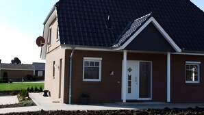 Una casa con techo de tejas oscuras, puerta blanca y un pequeño jardín.