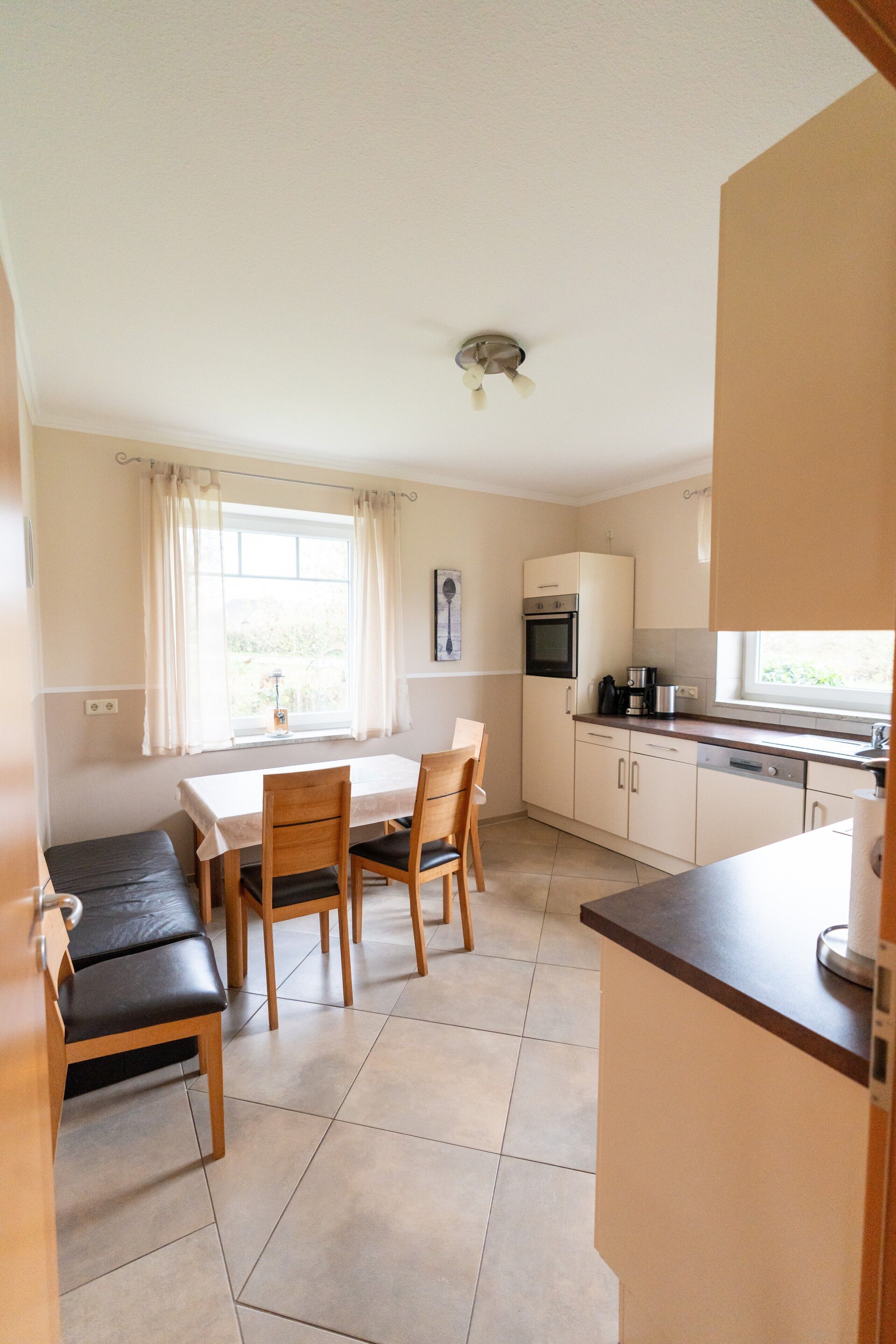 A compact kitchen with a dining area, featuring a table, chairs, a countertop, and a window with curtains.