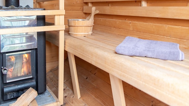 Un sauna de madera con estufa de leña, bancos y un cubo de madera.