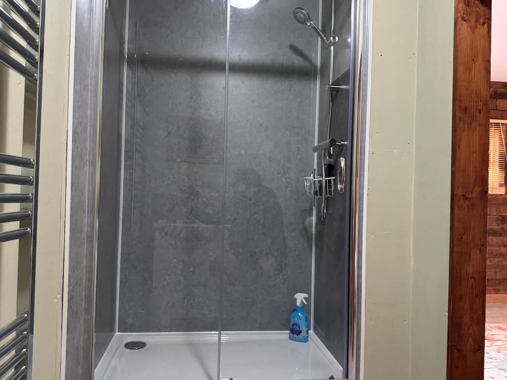 A glass-enclosed shower stall with a handheld showerhead and a bottle of liquid soap.