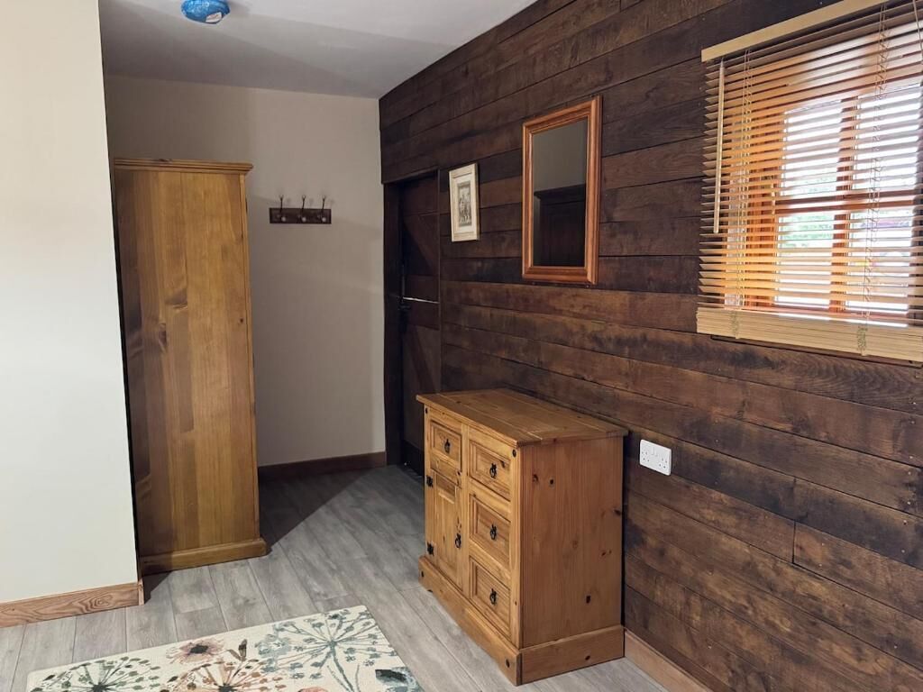A room with wooden panel walls, a wooden cabinet, a mirror, and a window with blinds.