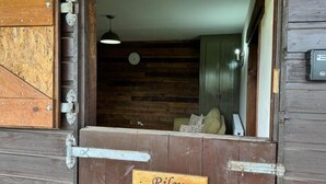 A rustic wooden door with a sign reading "Riley" and a view into a room with wooden walls and a hanging light fixture. - The Riley Stable- Cozy Getaway (Waterlooville)