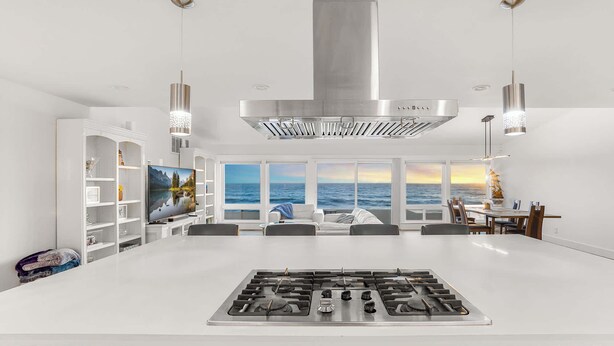 Una cocina moderna con una isla central, estantes empotrados y un amplio ventanal con vistas al océano.