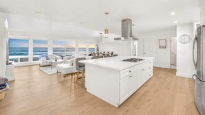 Una cocina moderna con una isla grande, armarios blancos y vista al océano a través de amplios ventanales.