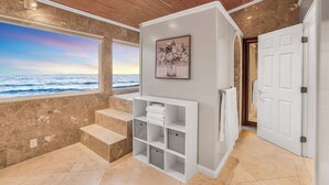 Un baño con un ventanal grande, un tocador blanco, un cuadro enmarcado y una puerta.
