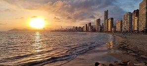 A coastal cityscape with a beach, high-rise buildings, and a sunset.