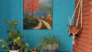A room with a blue wall, a painting of a forest path, a white cabinet with drawers, and a blue suitcase on the floor.