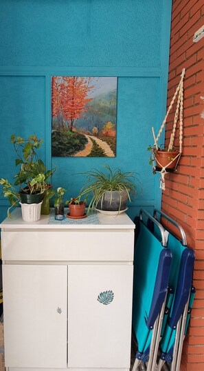 Une pièce avec un mur bleu, un tableau représentant un sentier de forêt, une armoire blanche avec des tiroirs et une valise bleue posée sur le sol.
