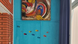 A room with a teal accent wall, a colorful abstract painting, a gray sofa, and a window with a blue curtain.