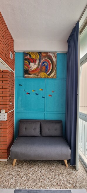 Une pièce avec un mur d’accent de couleur turquoise, un tableau abstrait aux couleurs vives, un canapé gris et une fenêtre avec un rideau bleu.