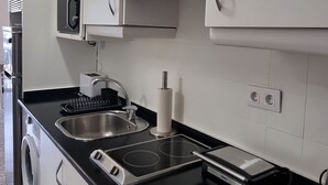 A compact kitchen with white cabinets, a black countertop, a microwave, a sink, and a built-in oven.