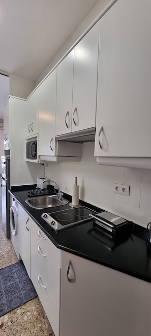 A compact kitchen with white cabinets, a black countertop, a microwave, a sink, and a built-in oven.